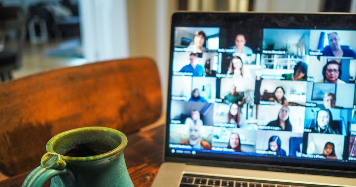 A laptop showing a video call with many participants, next to a green ceramic mug on a wooden table.