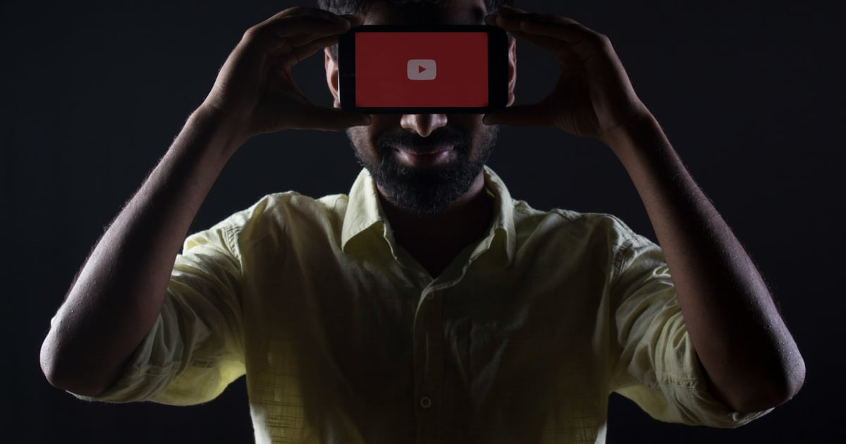 Man holding a phone showing the Youtube logo in front of his head.