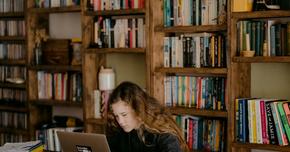 Young teen doing schoolwork at home by reading online on a laptop
