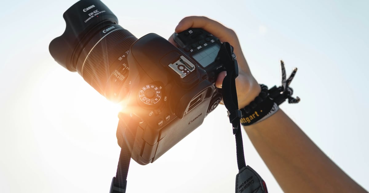 Hand holding a Canon DSLR camera up against a bright sunlit sky