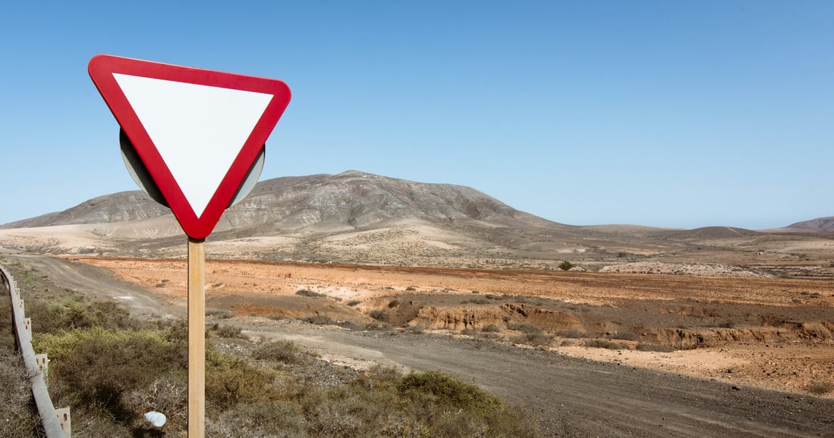 A blank yield sign stands beside a rural desert road with mountains in the background.