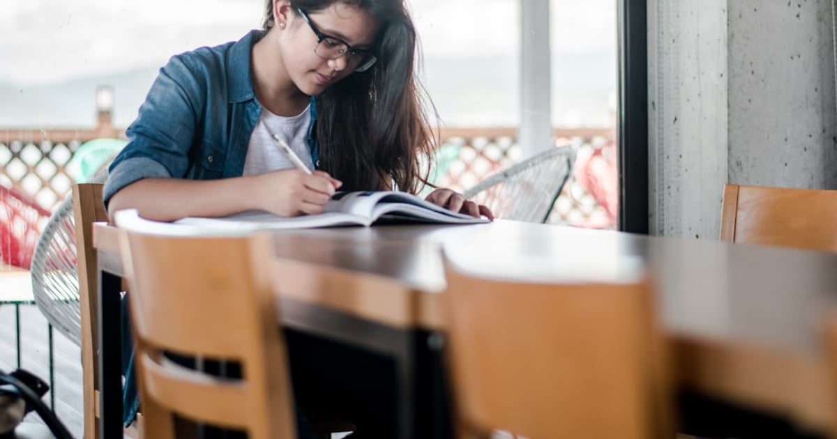 A student writing notes in a book while revising for an exam
